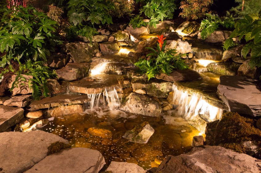 Water feature with dramatic underwater and landscape lighting illuminated at dusk